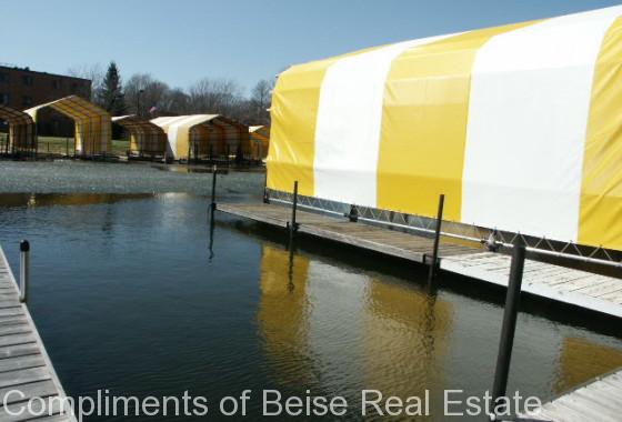 Yellow and white striped covered boat slips line the dock on calm water beneath a clear blue sky at Three Points Blvd. - Beise Real Estate