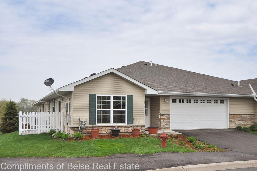 Charming single-story suburban house at 190 Kings Point with beige siding, green shutters, a white picket fence, two-car garage, and potted plants out front. Explore this gem in Kings Point real estate under an overcast sky. - Beise Real Estate