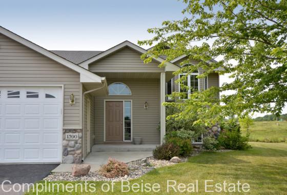 A beige suburban house at 1390 Waters Way features a brown front door, attached white garage, stone accents, and a landscaped front yard with a tree. House number 1390 is visible. - Beise Real Estate