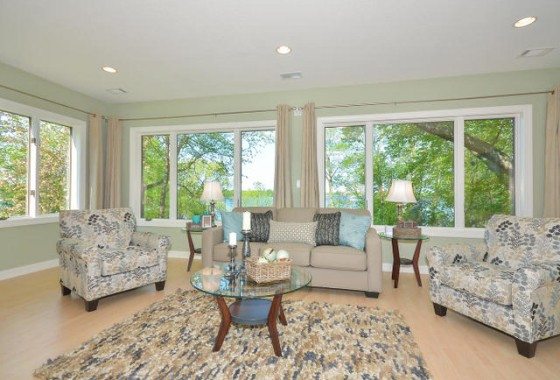 A bright living room with a beige sofa, two patterned armchairs, a glass coffee table, and large windows showcasing trees and Lake Sarah views—an inviting space in sought-after Lake Sarah real estate. - Beise Real Estate