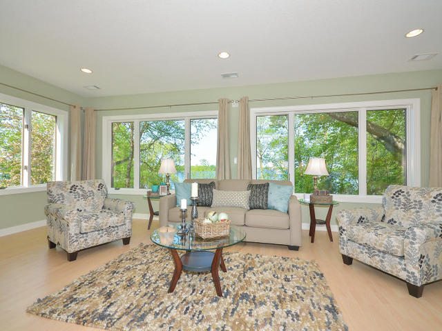 A bright living room with a beige sofa, two patterned armchairs, a glass coffee table, and large windows showcasing trees and Lake Sarah views—an inviting space in sought-after Lake Sarah real estate. - Beise Real Estate