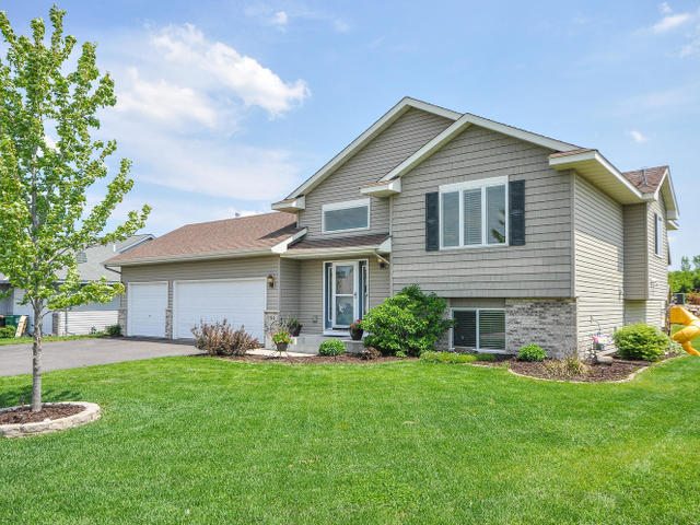 A two-story suburban house on Prairie Ridge Lane with gray siding, brick accents, a three-car garage, landscaped yard, and green lawn under a partly cloudy sky. - Beise Real Estate