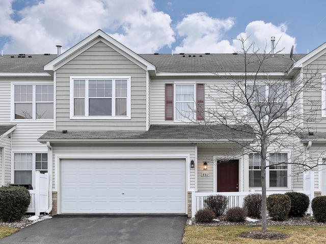 Charming two-story townhouse on Princeton Avenue with light gray siding, white trim, a red front door, double garage, driveway, small lawn, and bare tree in front beneath a partly cloudy sky. Ideal real estate opportunity!. - Beise Real Estate