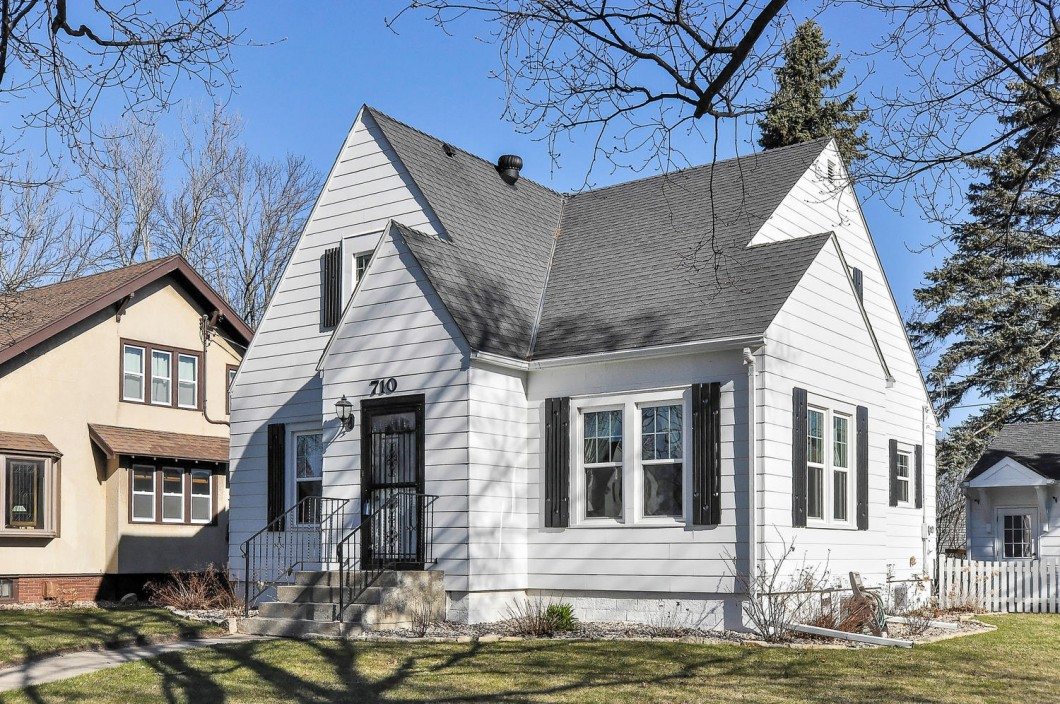 Charming white, single-family house at 710 Elm Street West with black shutters, steep gable roof, small front steps, and a manicured lawn, photographed on a clear day. - Beise Real Estate