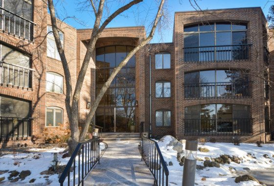 A brick apartment building with large windows and balconies on Laurel Avenue, a tree out front, snow on the ground, and a walkway leading to the main entrance. - Beise Real Estate
