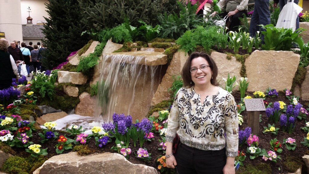 Kristin standing beside bright flowers at an indoor garden show.