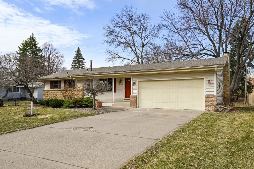 Single-story suburban house on Utah Avenue with light siding, red front door, attached two-car garage, concrete driveway, and leafless trees in the yard. Address 4709 New Hope. - Beise Real Estate