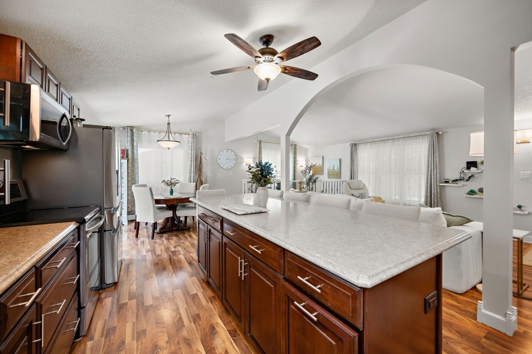A modern open-concept kitchen with dark wood cabinets, a large island, and an adjacent living and dining area featuring hardwood floors and neutral decor awaits you in Maple Plain on charming Rainbow Avenue. - Beise Real Estate