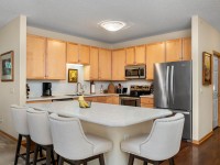 Modern kitchen in Unit 351 with light wood cabinets, stainless steel appliances, a center island with four upholstered chairs, and hardwood floors at 2150 Old School Road. - Beise Real Estate