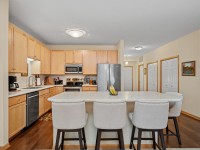 Modern kitchen in Unit 351 at 2150 Old School Road with light wood cabinets, stainless steel appliances, a large island with four upholstered chairs, and a bowl of bananas on the countertop. - Beise Real Estate