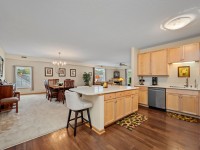 Open kitchen in Unit 351 with light wood cabinets and island, adjacent to dining and living areas with carpet and large windows at 2150 Old School Road, featuring a chandelier and elegant hardwood floors. - Beise Real Estate