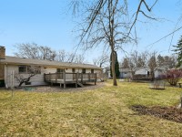 A single-story house on 4709 Utah Avenue with a wooden deck in a spacious backyard, scattered trees, and neighboring houses visible in the background. - Beise Real Estate