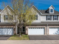 This Eden Prairie townhome features two stories, light siding with brick accents, three white garage doors, and a tree with sparse leaves in front. - Beise Real Estate
