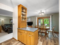 Open kitchen area with wooden cabinets, a dining table with chairs, large windows with curtains, and a view of the adjacent living room with a sofa and lamp. - Beise Real Estate
