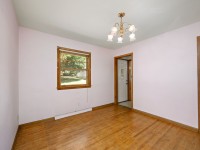 Empty room in Minnetrista at 4880 Grand View Avenue features light pink walls, hardwood floor, brass chandelier, wooden window with views of greenery, and a door leading to another area—a unique real estate opportunity. - Beise Real Estate