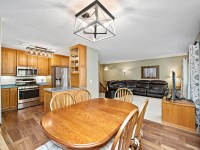 Open-concept kitchen, dining area, and living room featuring wood cabinetry, stainless steel appliances, a dining table, and a brown sectional sofa. - Beise Real Estate
