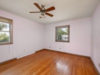 Empty room with light pink walls, two windows, a ceiling fan with lights, and hardwood flooring at 4880 Grand View Avenue in Minnetrista. - Beise Real Estate