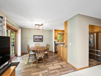 Dining area with a round wooden table and chairs next to a window; kitchen with stainless steel refrigerator and wood cabinets visible in the background. - Beise Real Estate