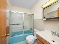 Charming small bathroom at 4880 Grand View Avenue, Minnetrista, featuring a sliding glass shower door, blue bathtub, white toilet, white sink with wooden vanity, and mirrored medicine cabinet—an inviting touch to this appealing real estate listing. - Beise Real Estate