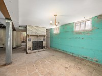 Unfinished basement at 4880 Grand View Avenue, Minnetrista, with turquoise painted cinderblock walls, tiled floor, two small windows, a brick fireplace, and exposed support beams. - Beise Real Estate