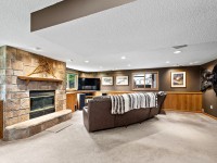 A cozy basement living room with a stone fireplace, large sectional sofa, TV, and wall-mounted art and bear rug, featuring carpeted floors and wood panel detailing. - Beise Real Estate