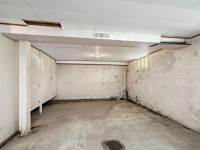 Unfinished basement room with concrete floor, exposed pipes, painted cinder block walls, and a single light fixture on the ceiling at 4880 Grand View Avenue, Minnetrista. Some areas show signs of wear and water damage in this real estate listing. - Beise Real Estate