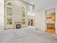 Spacious Eden Prairie living room with tall windows, carpeted floor, gas fireplace, and view into a kitchen with wooden cabinets; natural light fills the space on Wiedman Way. - Beise Real Estate
