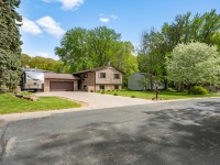 A split-level house with a two-car garage, RV parked on the driveway, and mature trees surrounding the property on a suburban street. - Beise Real Estate