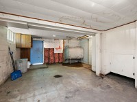 Unfinished basement room at 4880 Grand View Avenue in Minnetrista, featuring exposed pipes, oil tank, stained ceiling tiles, utility closet, garbage bins, and a blue door—a practical space for your real estate needs. - Beise Real Estate