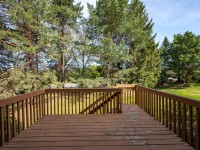 A wooden deck with railings on Wiedman Way overlooks a grassy yard and is surrounded by tall green trees under a clear Eden Prairie sky. - Beise Real Estate
