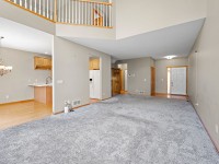 Spacious living area with gray carpet, beige walls, and a vaulted ceiling in this Eden Prairie home at 17595 Wiedman Way, adjacent to an open kitchen and dining area with wood flooring and a chandelier. - Beise Real Estate