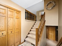 Carpeted staircase in a home entryway with wooden railings, double closet doors on the left, and a wreath hanging on the wall above. Tile and carpet flooring are visible. - Beise Real Estate