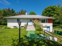 Charming single-story Minnetrista real estate features white siding with red accents, front steps to a blue door, lush green lawn, lamp post, and several trash bins on the right at 4880 Grand View Avenue. - Beise Real Estate