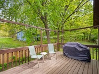 Wooden deck with two chairs and a covered grill, overlooking a fenced yard with green trees and a neighboring blue house in the background. - Beise Real Estate