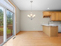 Kitchen and dining area with light wood floors, wooden cabinets, white countertops, chandelier, and sliding glass doors leading to a deck and green yard in the desirable Wiedman Way neighborhood of Eden Prairie. - Beise Real Estate