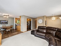 Open living space with brown leather sectional, dining table with chairs, wall clock, ceiling fan, and a view into the kitchen with stainless steel appliances. - Beise Real Estate