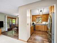 View of a kitchen with wooden cabinets and stainless steel appliances, adjacent to a dining area with sliding glass doors and a wall-mounted TV. - Beise Real Estate