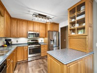 Modern kitchen with wooden cabinets, stainless steel appliances, granite countertops, built-in shelves with dishes, and a geometric overhead light fixture. - Beise Real Estate