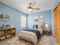 A child's bedroom with blue walls, a single bed, nightstand, bookshelves with toys, framed wall art, and a ceiling fan is virtually staged—creating a cozy space in this lovely home on Wiedman Way in Eden Prairie. - Beise Real Estate