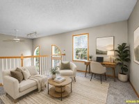 Loft area at Wiedman Way, Eden Prairie, with beige sofas, round coffee table, desk with chair and computer, large windows, indoor plant, and framed artwork. Room features carpet and white railing. Text: "Virtually Staged. - Beise Real Estate