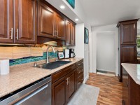 Modern kitchen on Rainbow Avenue with dark wood cabinets, marble countertops, a stainless steel dishwasher, colorful tile backsplash, coffee maker, and under-cabinet lighting—perfect for stylish Maple Plain living. - Beise Real Estate