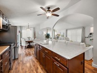 A modern open-concept kitchen with dark wood cabinets, a large island, and an adjacent living and dining area featuring hardwood floors and neutral decor awaits you in Maple Plain on charming Rainbow Avenue. - Beise Real Estate