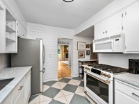 Modern kitchen with white cabinets, stainless steel refrigerator, gas stove, microwave, and marble countertops at 405 S Old Crystal Bay Road; doorway opens to living area with wood flooring and a fireplace. - Beise Real Estate