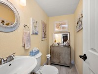 Charming small bathroom on Rainbow Avenue with yellow walls, a pedestal sink, toilet, decorative framed art, a mirror above a wooden cabinet, and a tissue box on the toilet tank. - Beise Real Estate