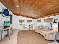Room at 405 S Old Crystal Bay Road in Orono features a wood plank ceiling, white paneled walls, a beige curved sofa, two chairs, desk with monitor, windows with woven shades, and a mounted fish decoration. - Beise Real Estate