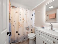 Charming small bathroom on Maple Plain with a floral shower curtain, white vanity and sink, toilet, mirror, and towels hanging neatly on the walls. - Beise Real Estate