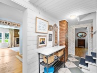 Bright hallway on Old Crystal Bay Road in Orono features a white shiplap wall, marble-topped console table, decorative mirror, brick column, framed art, and stairs with patterned tile floor. Living room is visible on the left. - Beise Real Estate