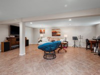 Spacious basement room with tile flooring on Rainbow Avenue, Maple Plain, featuring a sofa, round chair, TV, musical instruments, desk, and wall art. - Beise Real Estate