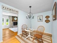 Small dining area with two wooden chairs and a round table set for two, beneath a black chandelier. Wall art and a "Farmhouse" sign decorate the light blue room in this charming Orono home on Old Crystal Bay Road. - Beise Real Estate