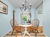 A small round table with two wooden chairs sits under a black chandelier in a light blue dining area with a striped rug and wall art, creating a cozy Orono retreat at 405 S Old Crystal Bay Road. - Beise Real Estate
